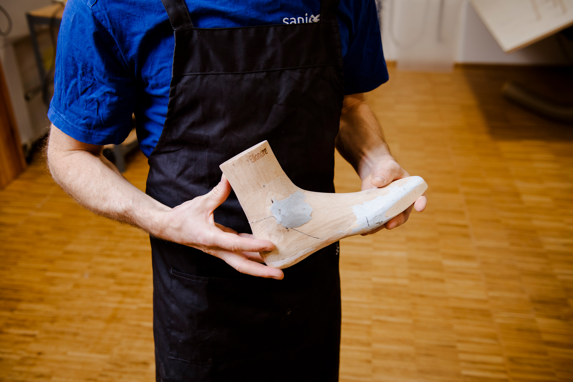 Ein Schuhmacher hält auf dem Bild ein Holzmodell eines Fußes in der Hand.