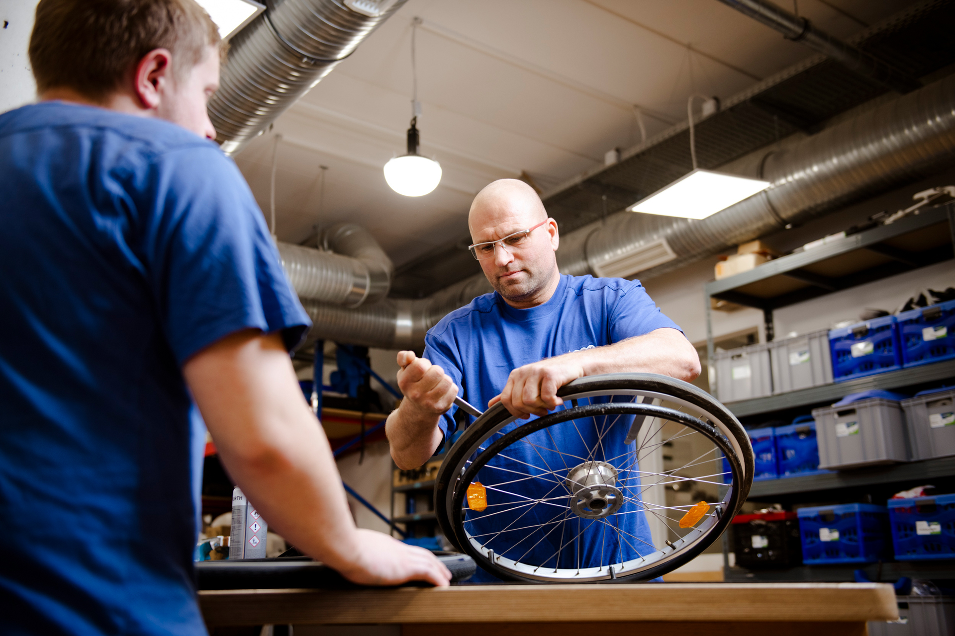 Zwei Männer sind dabei, an einem Rollstuhl zu arbeiten. Einer von ihnen kümmert sich um ein Rad.