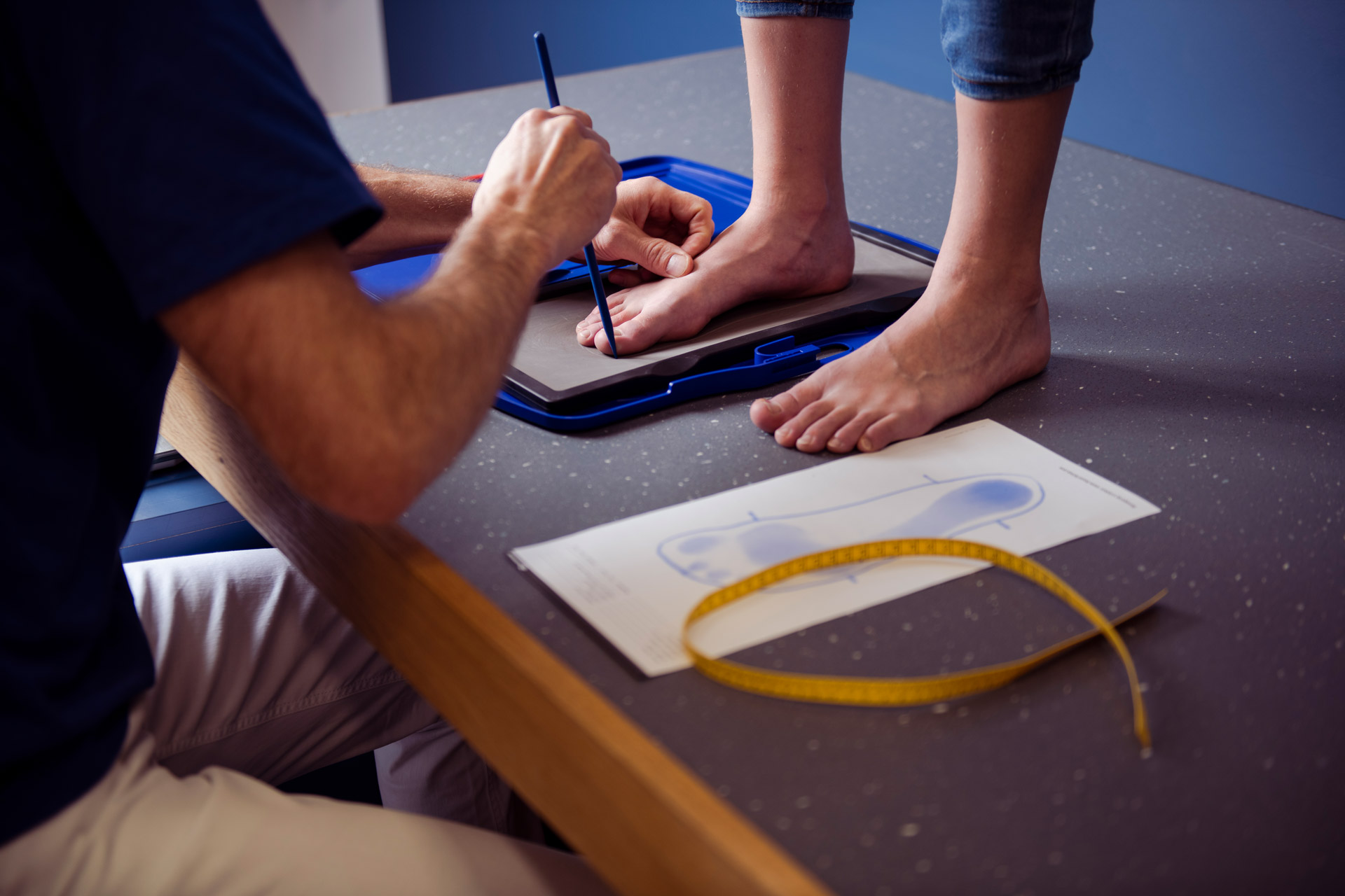Das Bild zeigt einen Kinderfuß auf einer Matte, die einen Abdruck nimmt, während eine Fachkraft den Fuß umzeichnet.