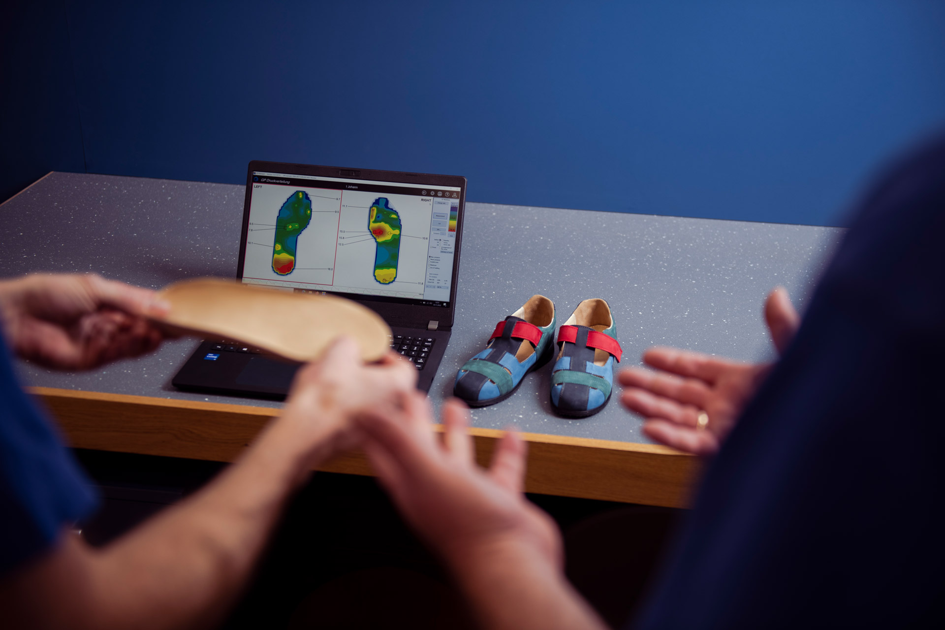 Auf dem Bild sind zwei Fachleute zu sehen, die eine Einlage für diabetisadaptierte Schuhe überprüfen. Im Hintergrund ist ein Monitor mit Einlagen, auf denen verschiedene Druckpunkte markiert sind.